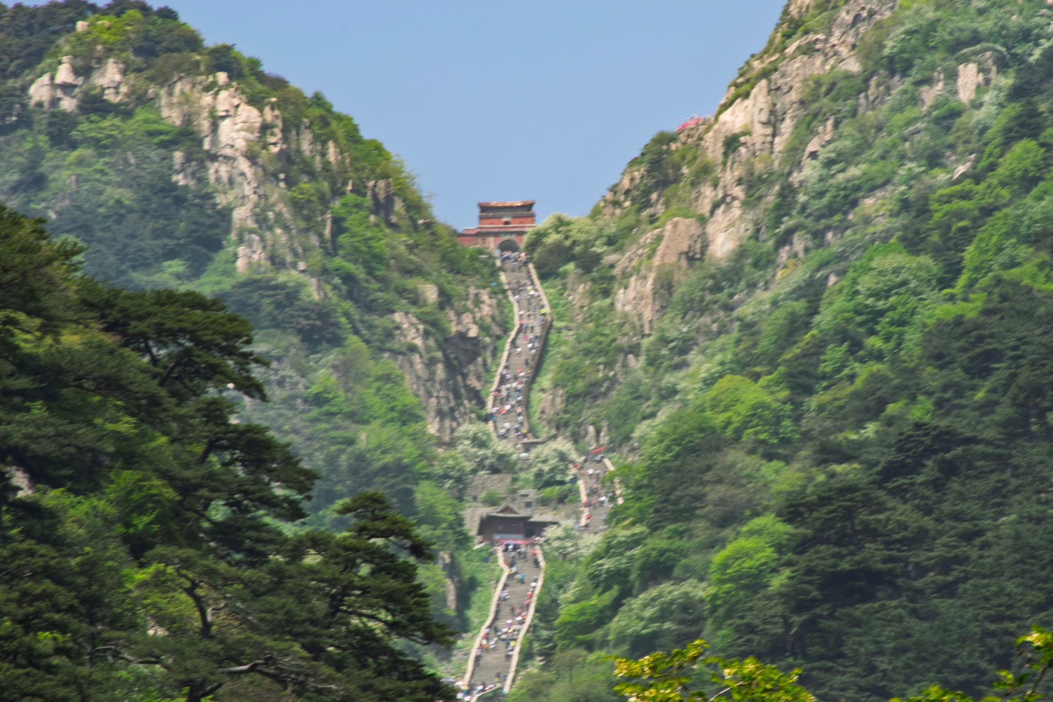 陡峭的石阶从山脚一直延伸到山顶,山顶有一座小建筑,周围是茂密的绿色植被。